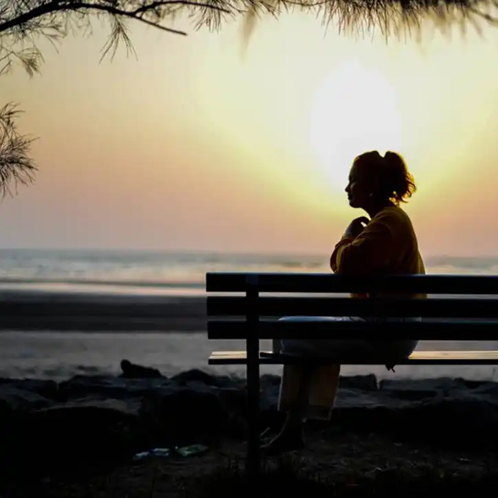 Woman sitting alone at sunset, pausing to calm anxiety through quiet reflection